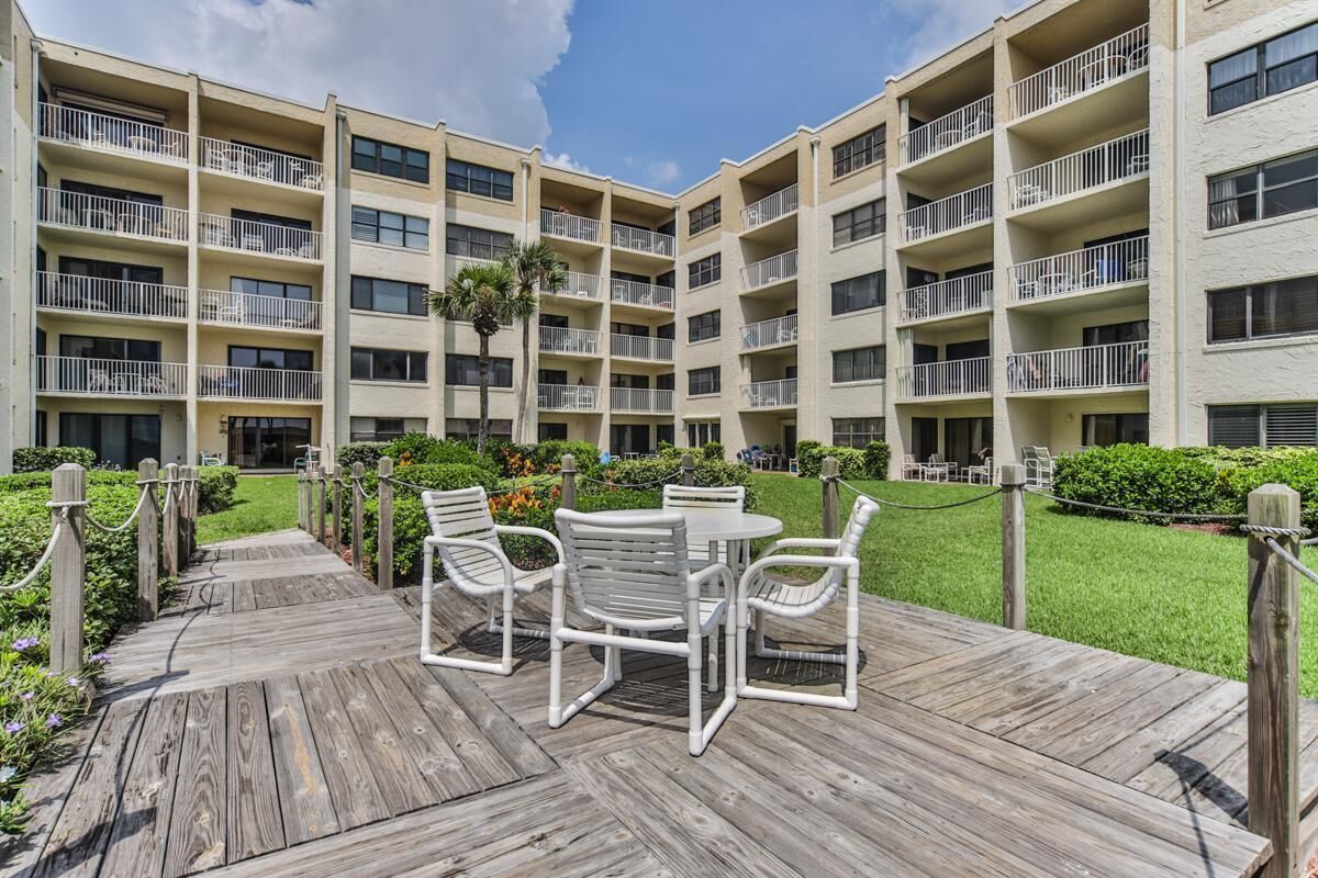 Un hotel de varios pisos con balcones, una terraza de madera con mobiliario exterior y un césped bien cuidado.