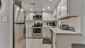 A modern kitchen with stainless steel appliances, white cabinetry, and a tiled backsplash.