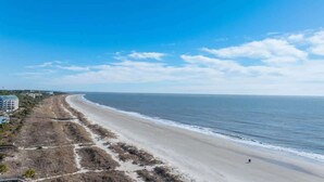 A beach with a clear sky, a sandy shore, and a few buildings in the background. - Admiral’s Row 203: Romantic Oceanfront Retreat with Bunk Beds (Hilton Head Island)