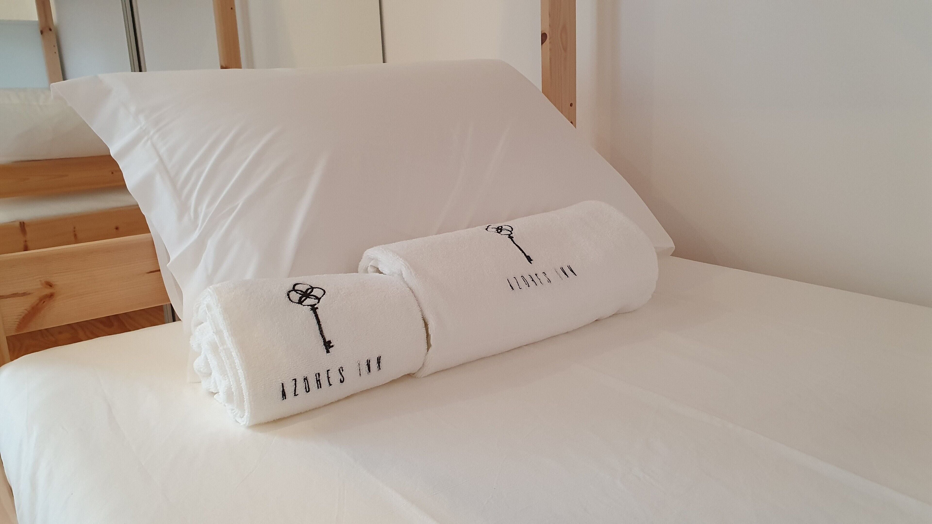 A neatly made bed with white linens and pillows, featuring embroidered text and a key design.