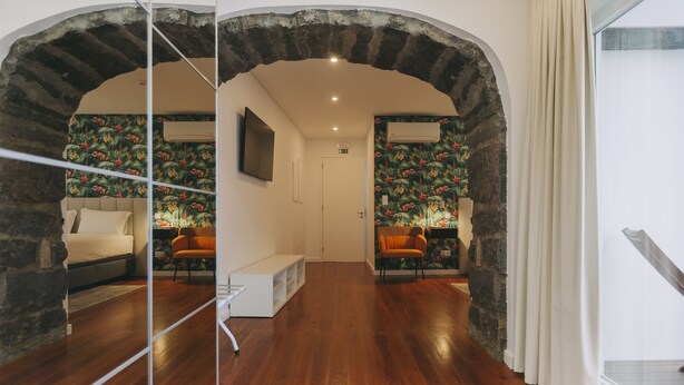 Eine Hotelhalle mit Holzboden, Steinbögen, einer Couch, einem orangefarbenen Sessel und einem an der Wand befestigten Fernseher.