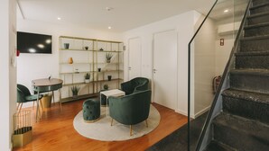 Ein modernes Wohnzimmer mit einem runden Couchtisch, zwei grünen Sesseln, einem weißen Sofa und einer Glasstufenkonstruktion.