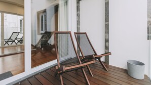 Eine Holzterrasse mit zwei Korbstühlen und einer grauen Mülltonne.