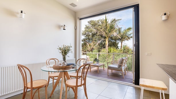 Een moderne kamer met een glazen tafel, houten stoelen, een klein bijzettafeltje en uitzicht op een tuin door een schuifpui.