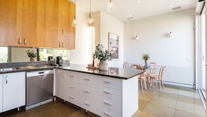 Een moderne keuken met houten kastjes, een centraal eiland met lades, een ingebouwde vaatwasser en een eethoek met tafel en stoelen.