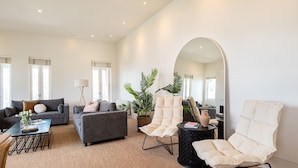 Een moderne woonkamer met een grijze bank, een witte fauteuil, een ronde tafel en een grote spiegel.
