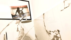 A bathroom with a marble wall, a framed photo, and a showerhead.