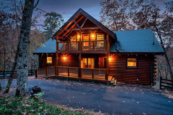 A log cabin with a balcony, a covered porch, and a driveway.