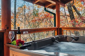 A wooden deck with a hot tub, a wine bottle, and glasses.