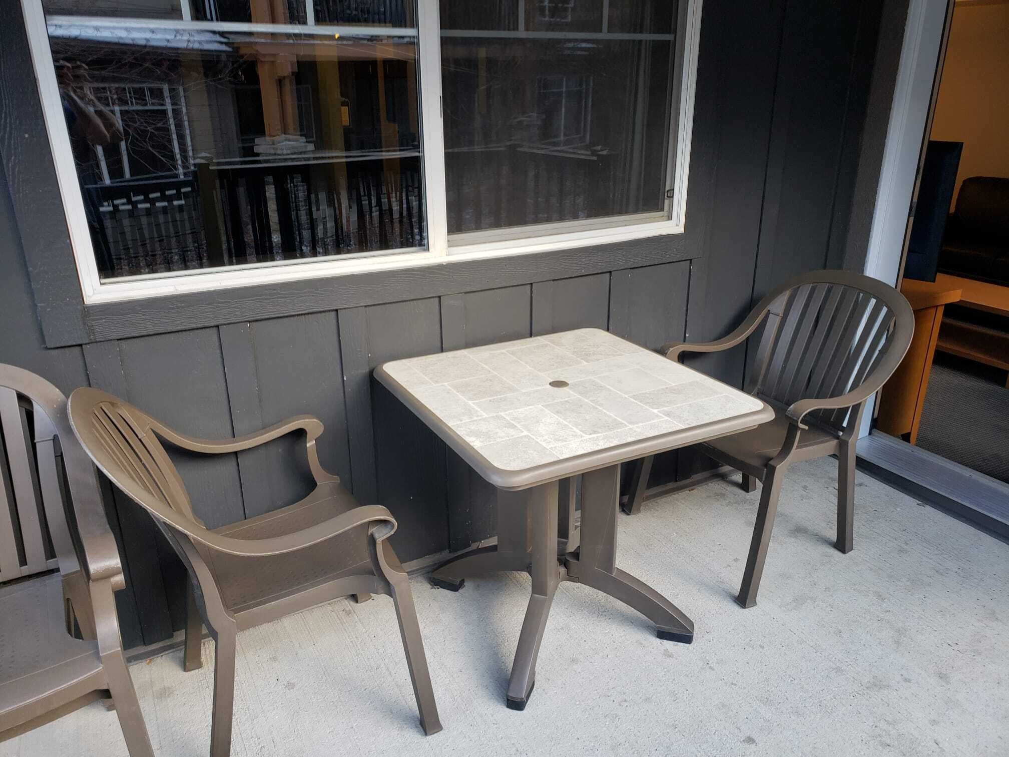 Un pequeño espacio al aire libre con una mesa y dos sillas, una ventana y una puerta.