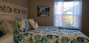 A bedroom with a bed featuring a fish pattern bedspread, a white headboard, and a window with blinds. - Peaceful view of Paradise in the Mountains (Candler)