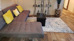 Ein braunes Sofa mit gelben Kissen, ein schwarzer Hocker und ein dekoratives Metallregal mit Flaschen und Pflanzen.