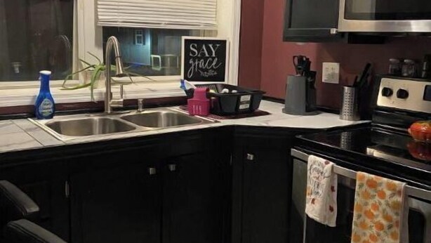 A kitchen with black cabinets, a stainless steel stove, and a microwave. There is a window with blinds and a sign that says "Say Grace". - Browns Creek Getaway (Marlinton)