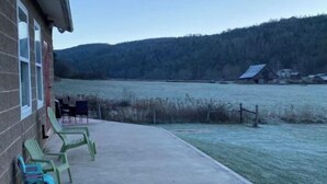 A building with a concrete patio, outdoor seating, and a view of a lake and forested hills. - Browns Creek Getaway (Marlinton)