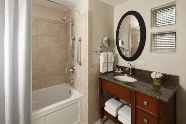 A bathroom with a bathtub, a sink, a vanity with a mirror, and a shower with grab bars.