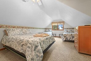 A bedroom with a large bed, a smaller bed, a dresser, and a window with curtains.