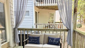 A covered porch with a sofa, chairs, and a table. - Cheerful Sound Side Condo (Kill Devil Hills)