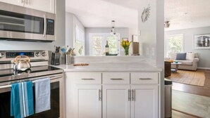 A modern kitchen with white cabinetry, stainless steel appliances, and a large island. - Cheerful Sound Side Condo (Kill Devil Hills)