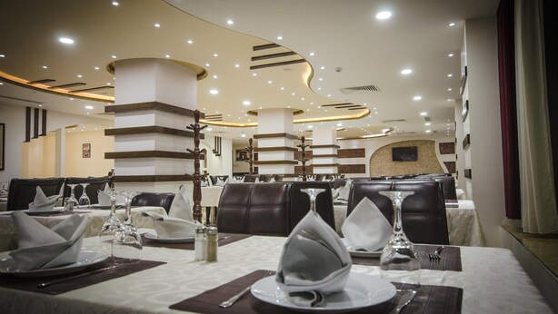 A restaurant with multiple dining tables set with white tablecloths, silverware, and glassware. The ceiling features recessed lighting and decorative columns. - Hotel Elbey Constantine (Constantine)
