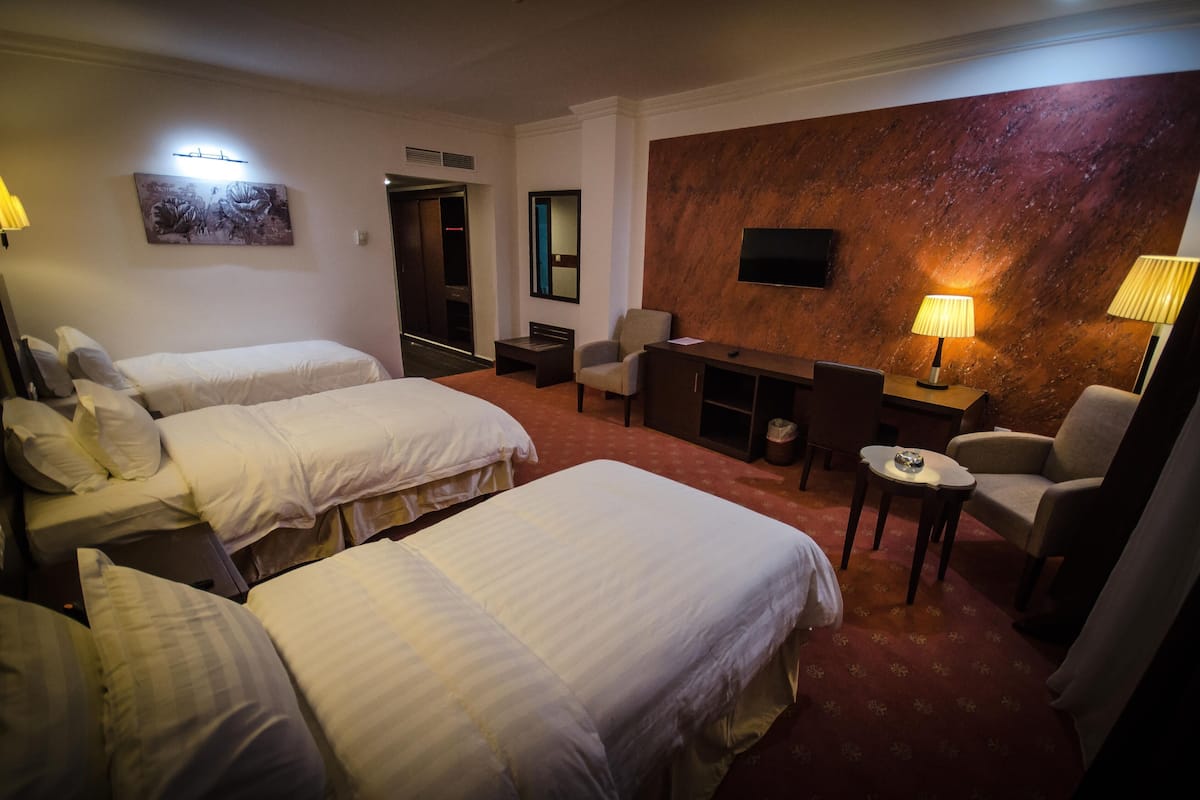 A hotel room with two beds, a desk, a chair, a TV, and a wall-mounted artwork.