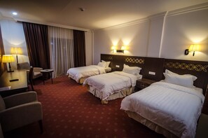 A hotel room with three beds, a desk, and two lamps.