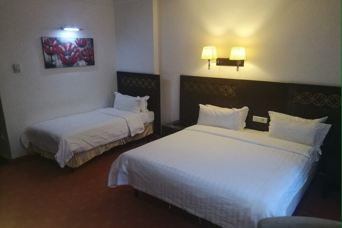 A hotel room with two beds, a painting on the wall, and two wall-mounted lamps.