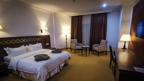 A hotel room with a large bed, two armchairs, a small table, and a desk with a lamp. - Hotel Elbey Constantine (Constantine)