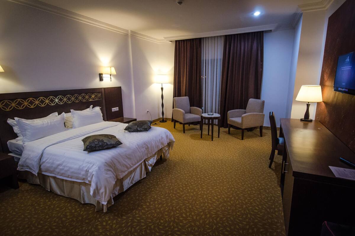 A hotel room with a large bed, two armchairs, a small table, and a desk with a lamp.