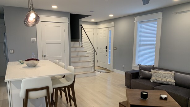 A modern living room with a dining area, a staircase, and a large window with blinds. - Luxury modern house  off Thames Street (Newport)