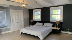 A bedroom with a large bed, two bedside tables with lamps, a door, and two windows. - Luxury modern house  off Thames Street (Newport)