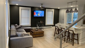 A modern living room with a sectional sofa, a coffee table, a TV, and a dining area with bar stools. - Luxury modern house  off Thames Street (Newport)