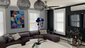 A modern living room with a sectional sofa, a dining table, pendant lights, a ceiling fan, a large TV, and a colorful abstract painting. - Luxury modern house  off Thames Street (Newport)