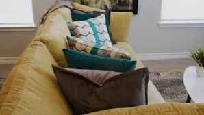 Ein Wohnzimmer mit einer Couch, Kissen, einem gerahmten abstrakten Gemälde und einem kleinen Tisch mit einer Pflanze.