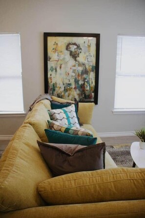 A living room with a sofa, pillows, a framed abstract painting, and a small table with a plant. - Downtown Duplex-San Antonio Unit #2 (San Antonio)