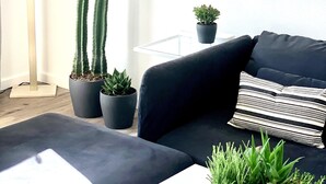 A modern living room with a black sofa, a striped pillow, and two potted plants. - NEW! Joshua Tree Dream - A Modern Desert Spa Retreat (Twentynine Palms)