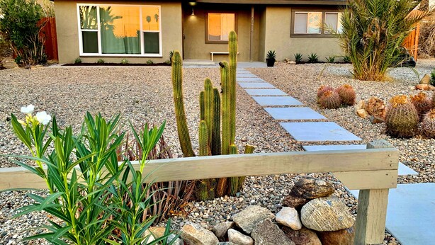 A modern house with a gravel driveway, a wooden fence, and various cacti and succulents in the garden. - NEW! Joshua Tree Dream - A Modern Desert Spa Retreat (Twentynine Palms)