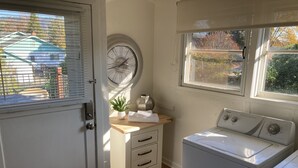 Une buanderie équipée d’un lave-linge, d’un étendoir, d’un petit évier et d’une fenêtre avec des stores.