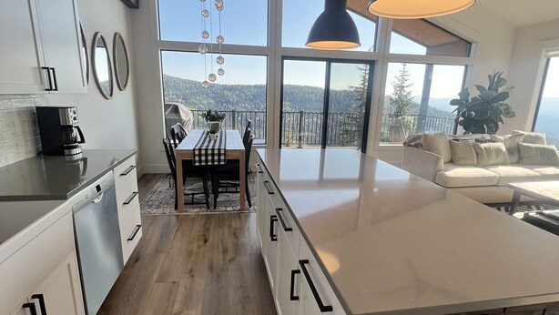 Eine moderne Küche mit einer großen Kochinsel, Holzböden und Blick auf eine bewaldete Landschaft durch große Fenster.
