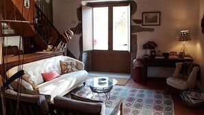 Una sala de estar acogedora con un sofá blanco, una mesa de centro de vidrio y un tapete estampado. Se ve una escalera al fondo, que sube a un piso superior.