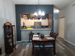 Un coin repas avec une table et des chaises en bois, un lustre et une cuisine en arrière-plan.