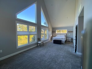 A spacious bedroom with large windows, a bed, a chair, and a small table.