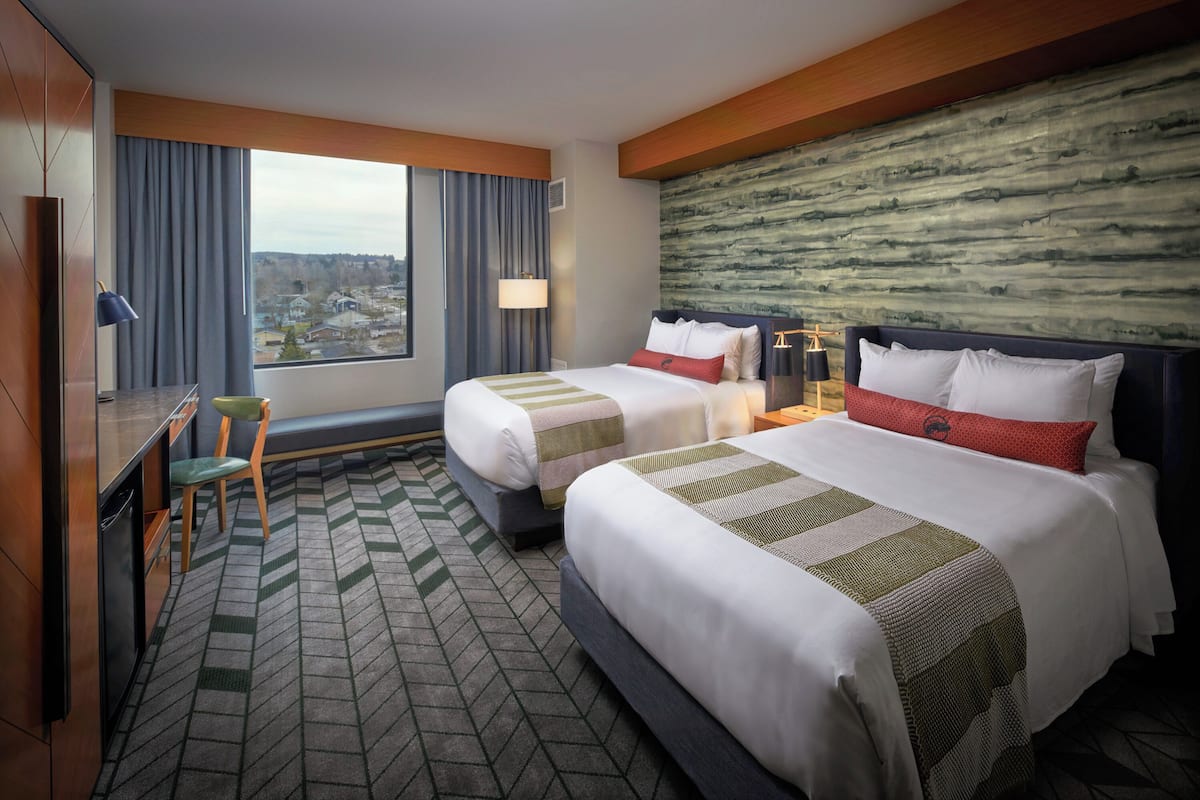 Ein Hotelzimmer mit zwei Betten, einem Schreibtisch, einem Stuhl und Blick auf die Stadt.