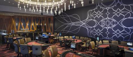 A casino area with multiple blackjack tables, chairs, and a large illuminated sign.