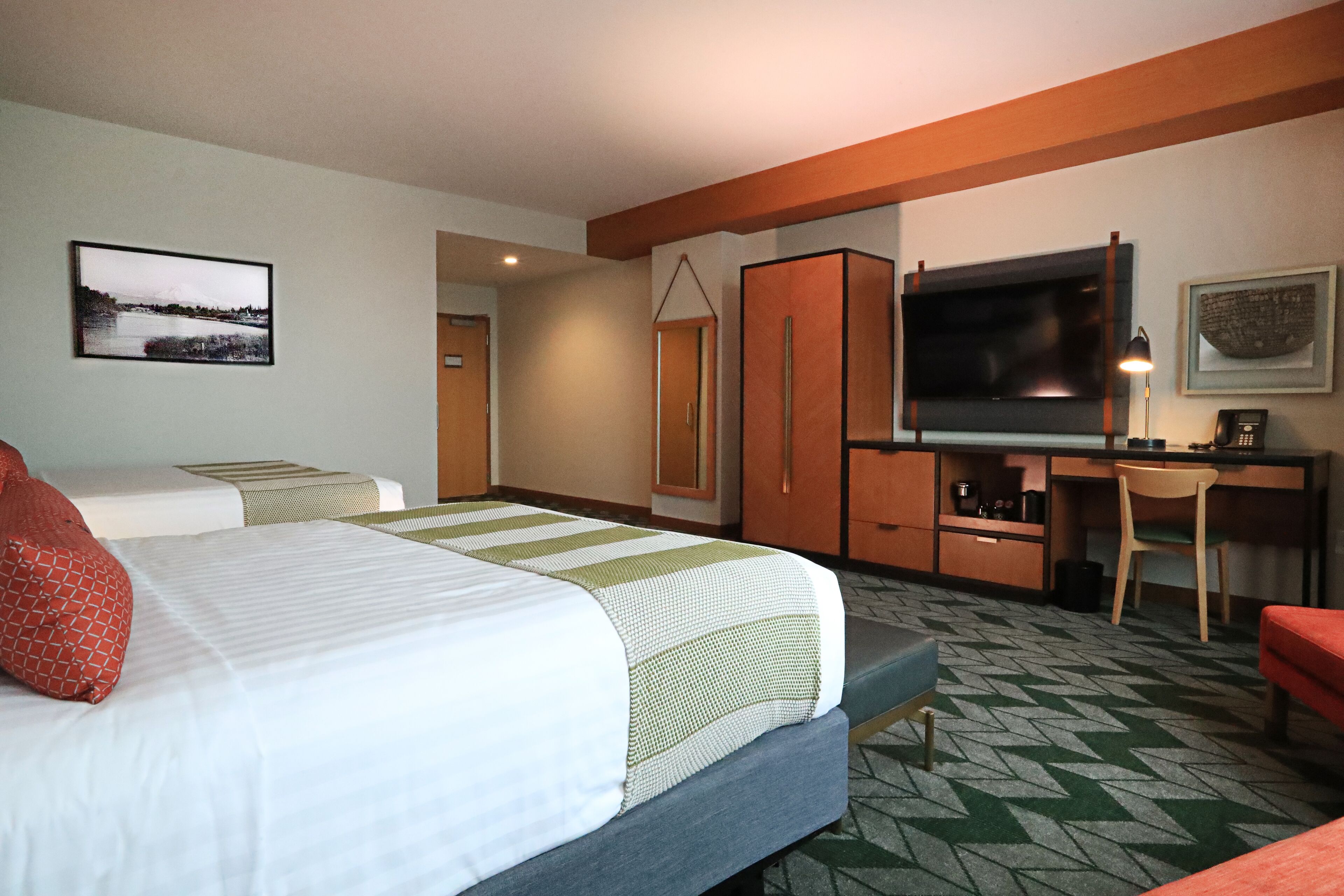A hotel room with two beds, a desk, a TV, and a chair.