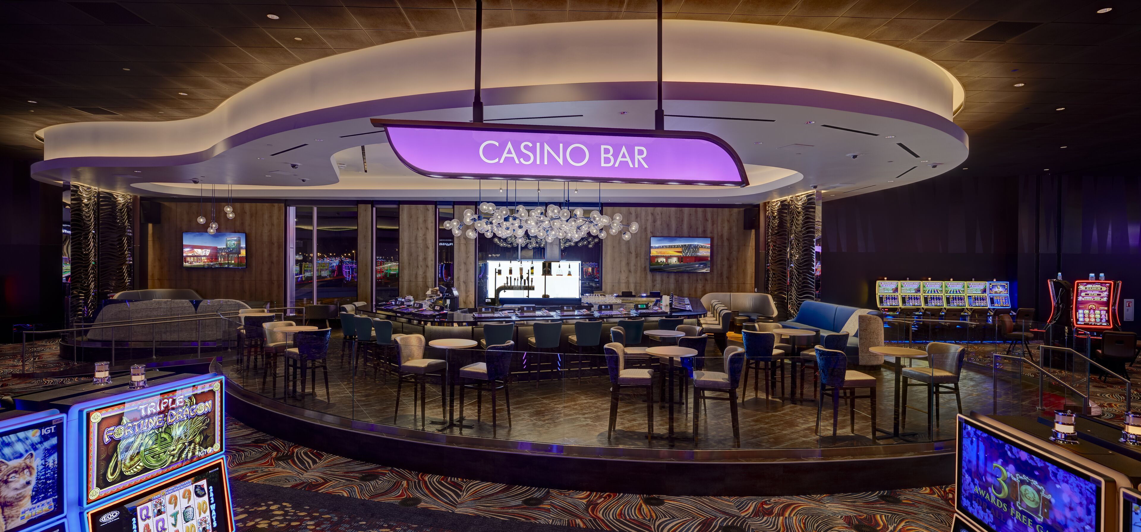 Un bar de casino doté d’un plafond incurvé, de plusieurs écrans et de différents types de sièges, notamment des tables et des chaises.