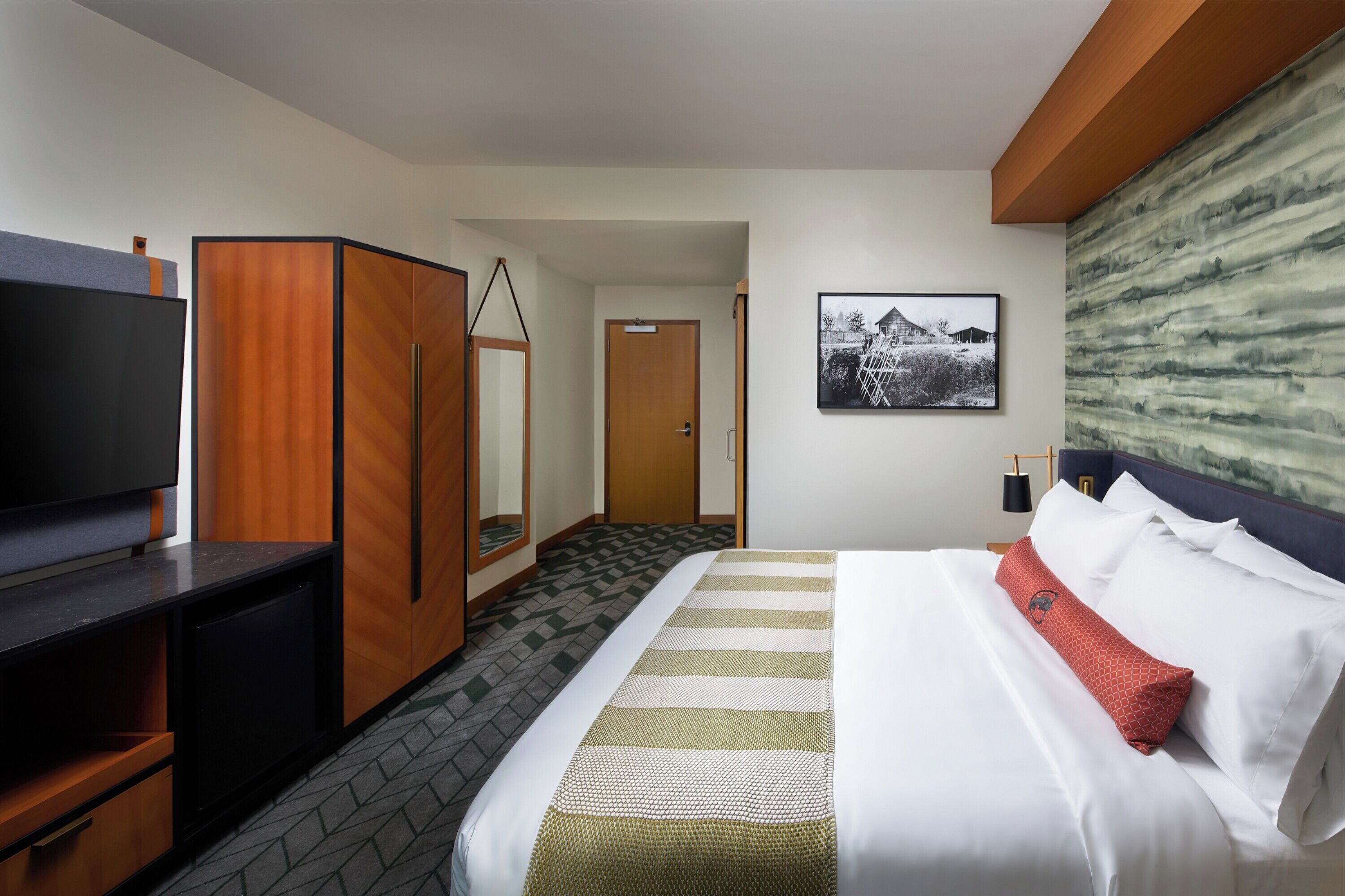 Habitación de hotel con cama, televisor, armario y un cuadro en la pared.