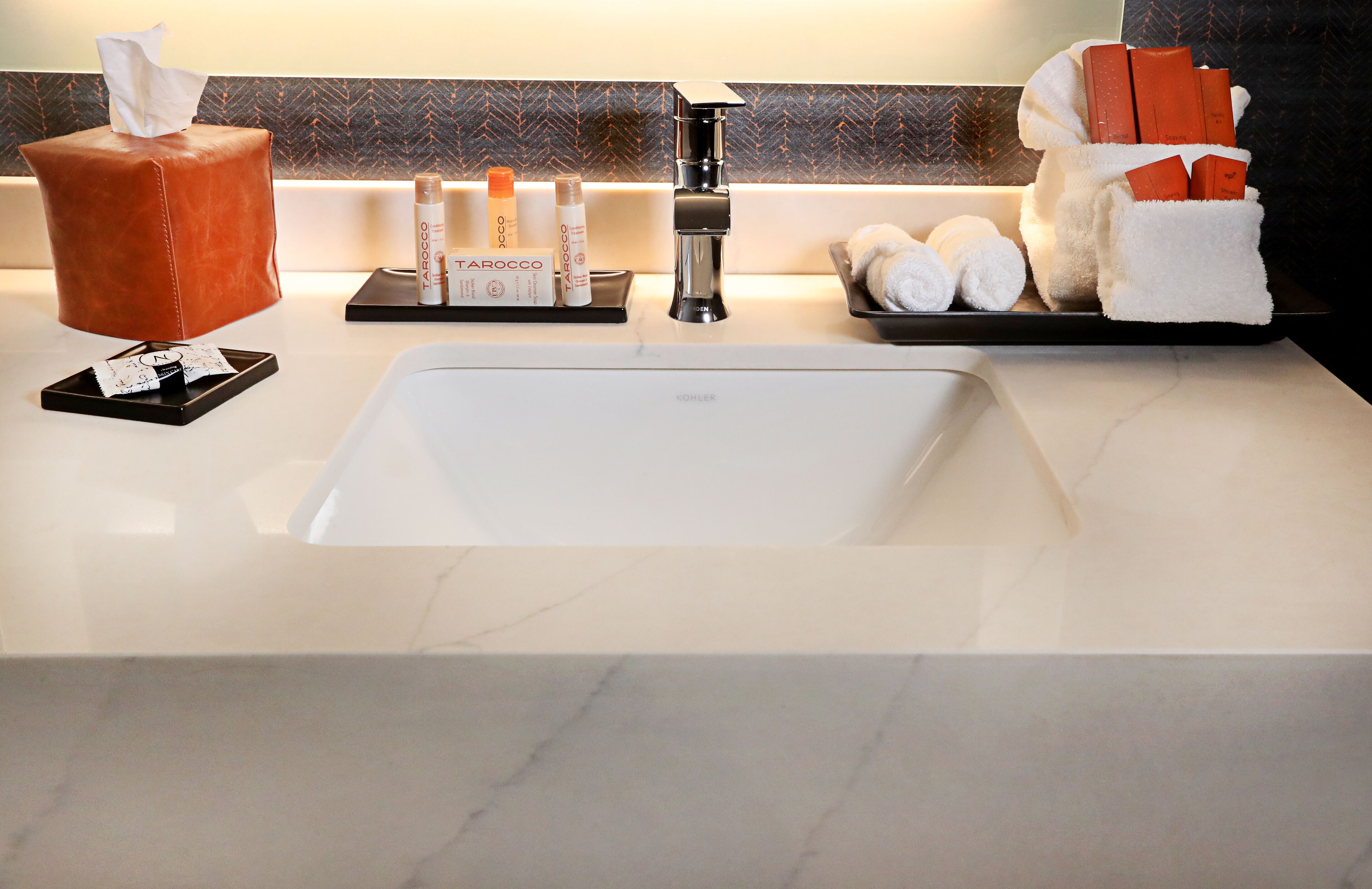 A hotel bathroom with a marble sink, a tissue box, toiletries, and towels.
