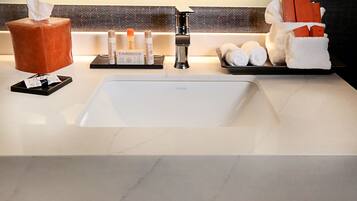 A hotel bathroom with a marble sink, a tissue box, toiletries, and towels.