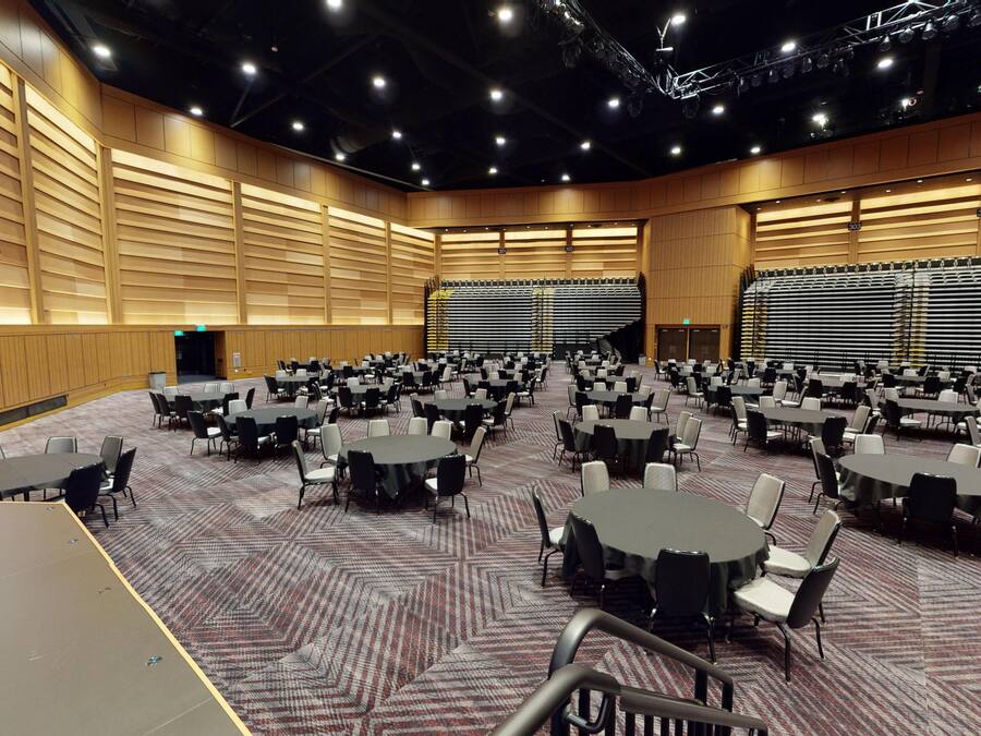 A large conference room with multiple tables and chairs, a stage, and a large sign with 'QC' on the left.