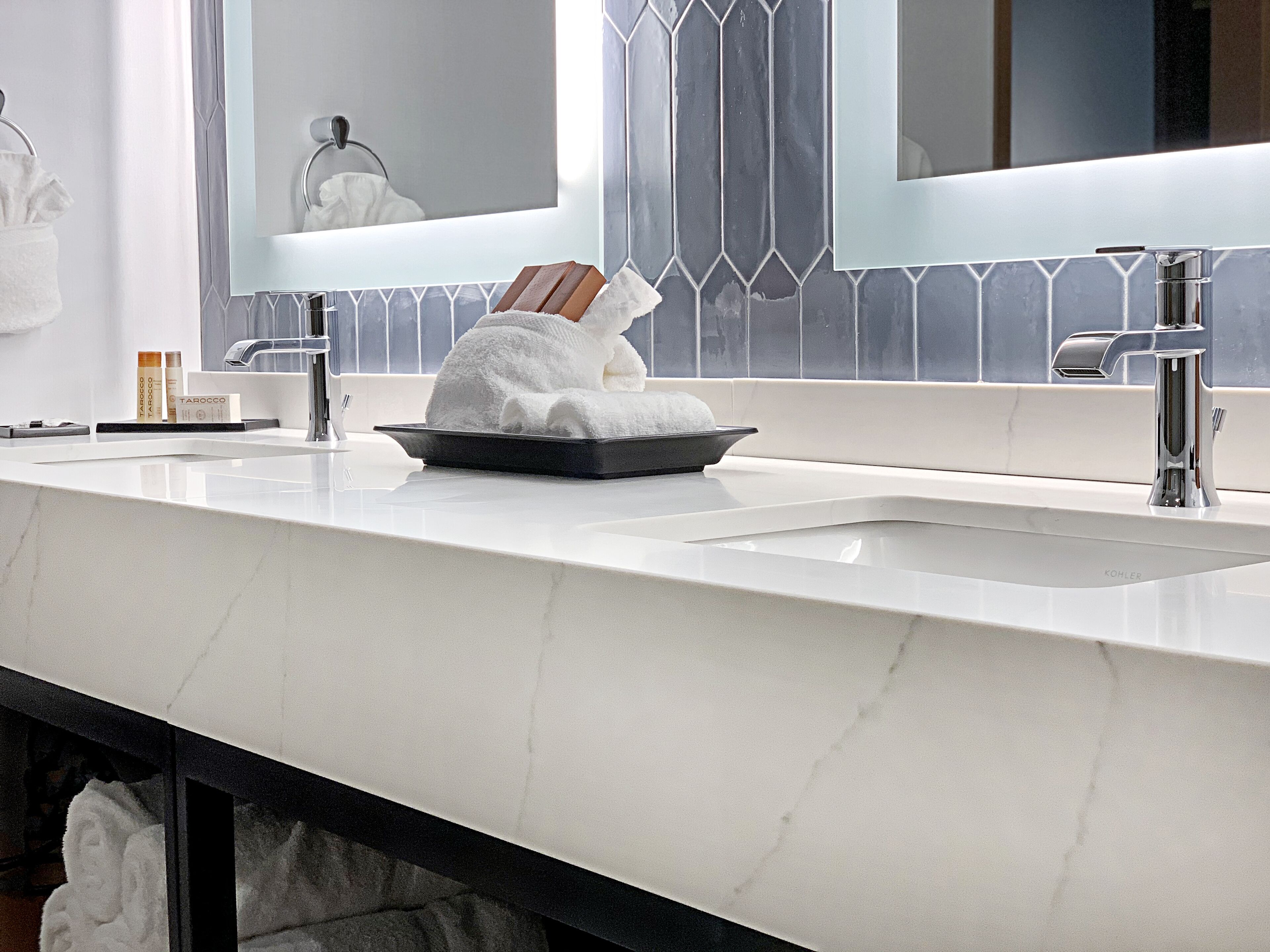 A bathroom with a white marble sink, a mirror, and a towel rack.